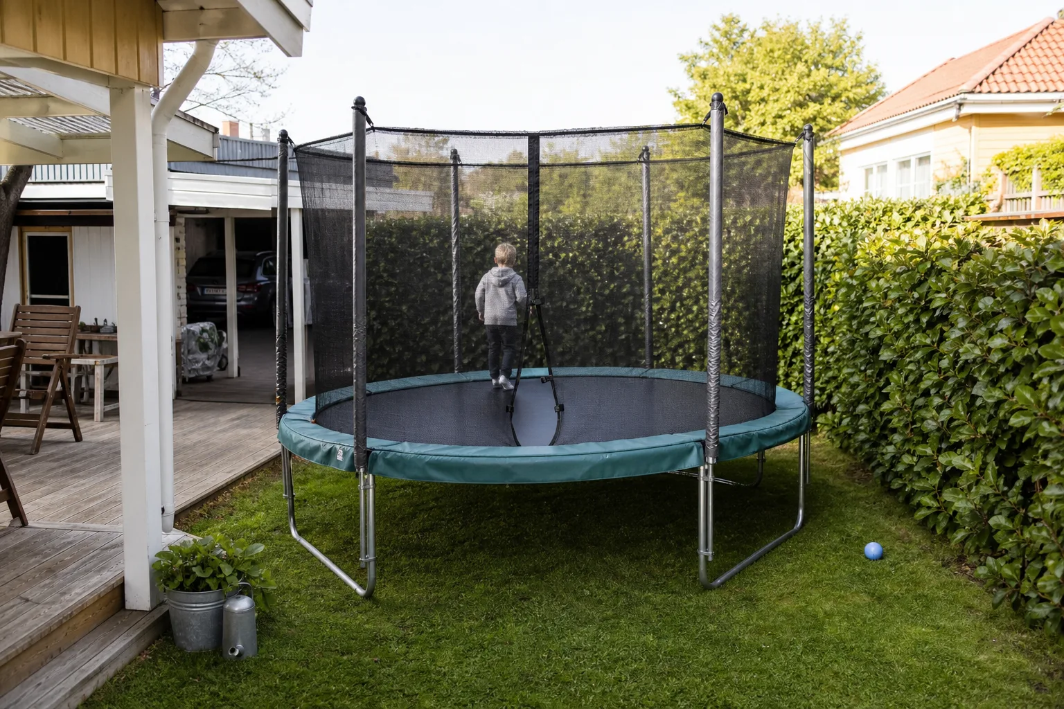 Liten studsmatta mellan altan och häck i villaträdgård