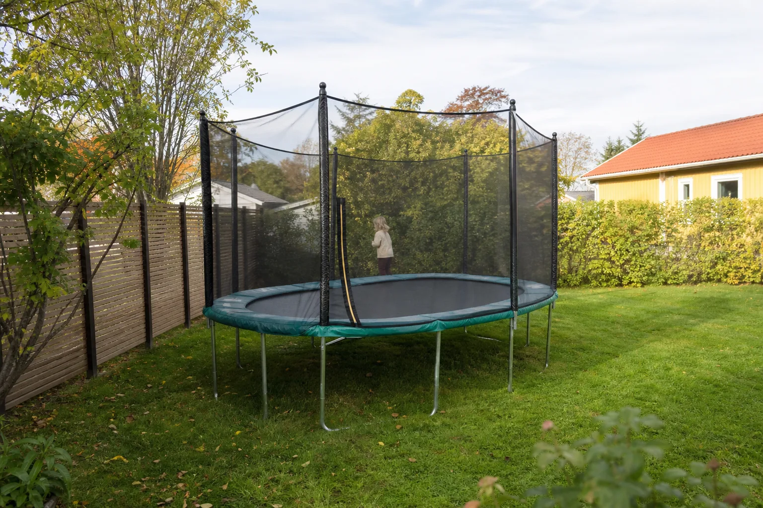 Oval studsmatta på avlång gräsmatta vid trästaket